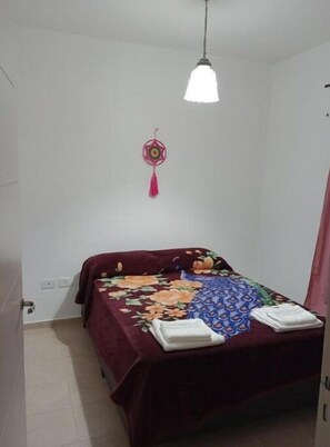 Un dormitorio con una cama cubierta con una colcha estampada, un adorno colgante y una lámpara de techo blanca.