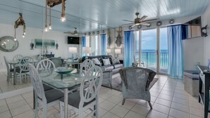A spacious living area with a dining table, chairs, and a sofa. There are ceiling fans, large windows with curtains, and a view of the ocean. - Seaglitz - 2 bed 2 bath Oceanfront (Miramar Beach)