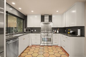 Enjoy cooking in this kitchen with oven and range hood, complemented by white cabinetry and a black countertop.