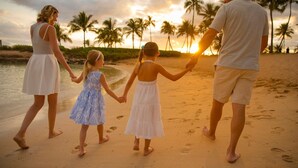 Eine Familie geht am sandigen Strand entlang, im Hintergrund Palmen und das Meer.