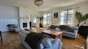 A spacious living room with a fireplace, a piano, and a large window with curtains. - Beautiful lake view house  (Vasteras)