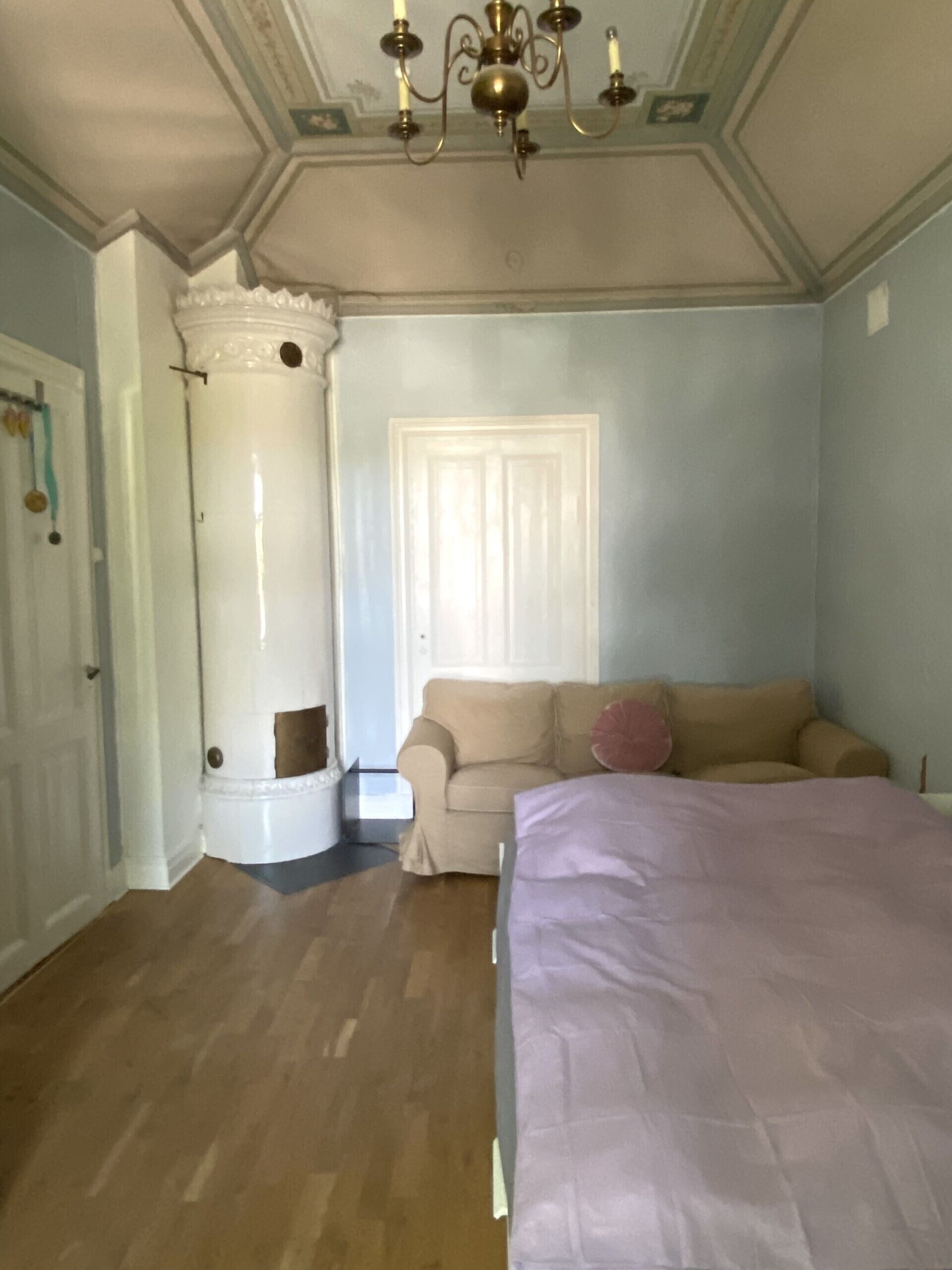 Una stanza con un letto grande, un divano beige, una colonna bianca e un lampadario.