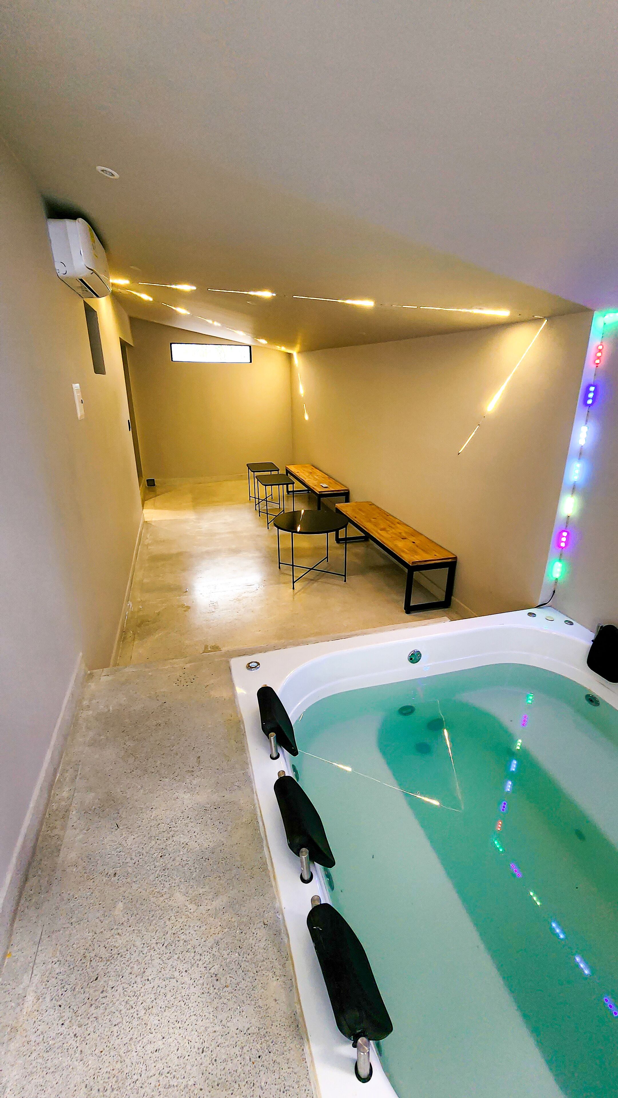Una habitación con un jacuzzi, un banco de madera y una mesa con sillas.