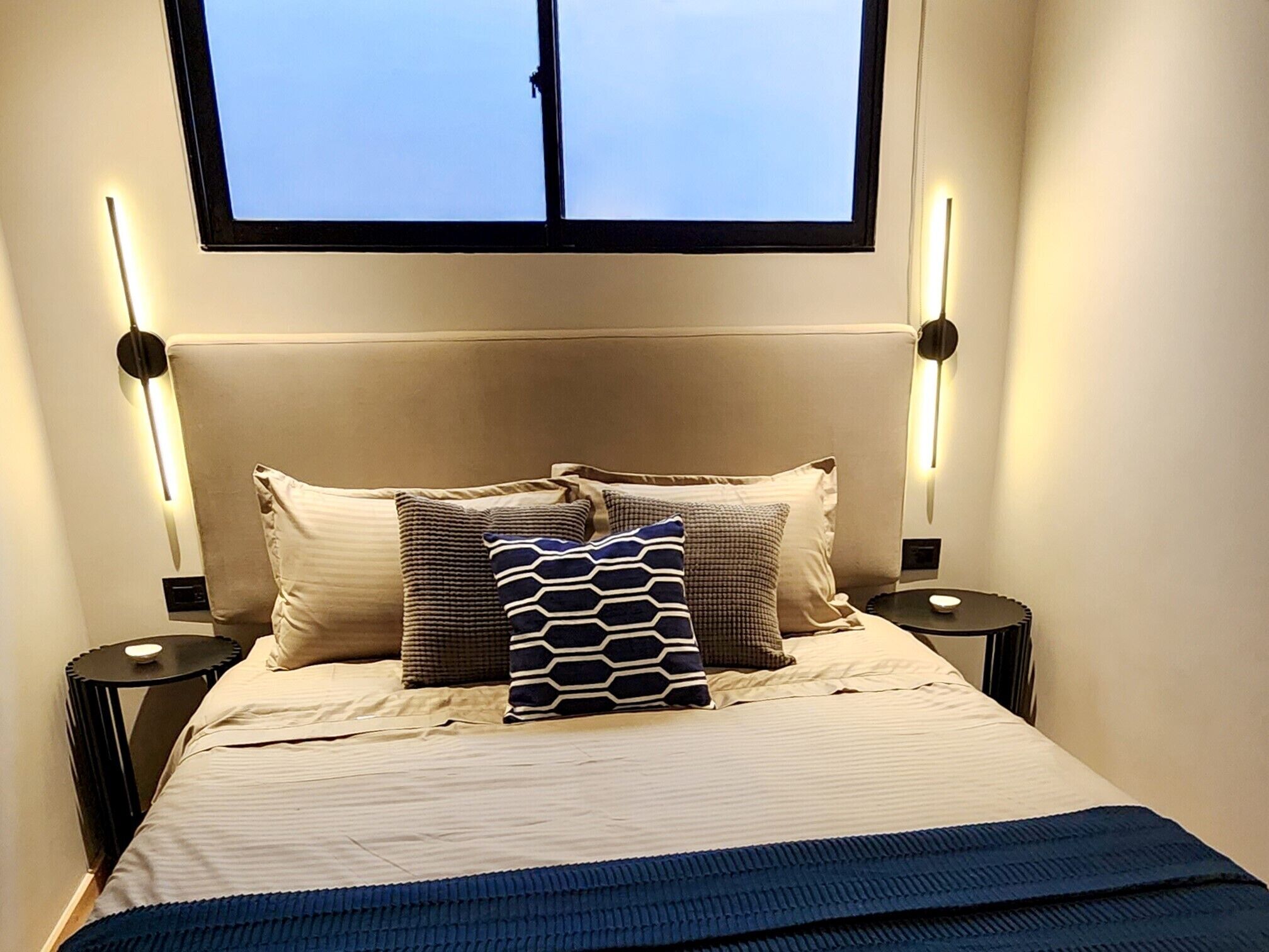 Un lit bien fait, recouvert d’une couverture à rayures, deux tables de chevet avec des lampes et une fenêtre au-dessus du lit.
