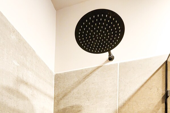 A showerhead with a circular black head and multiple holes, mounted on a wall with a textured beige tile design.