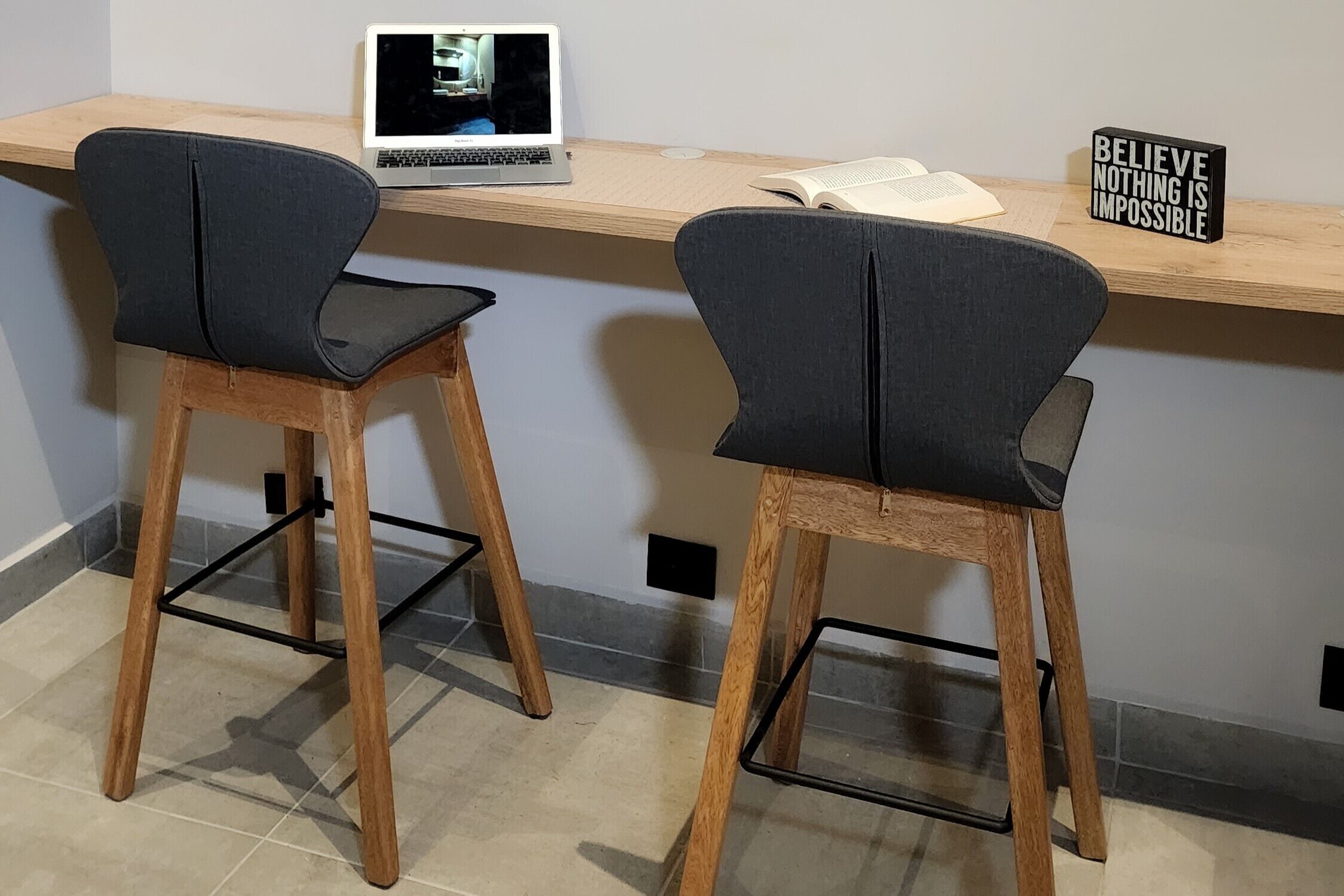 Two high chairs with wooden legs and black seats, a laptop on a wooden desk, and a motivational sign on the desk.