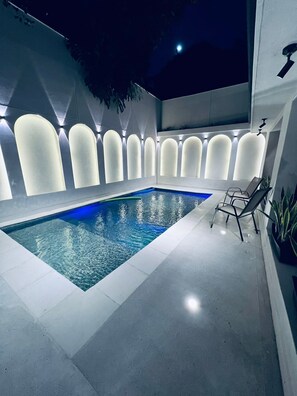 A modern indoor swimming pool with a clear blue water feature, surrounded by a sleek, white tiled floor and walls.