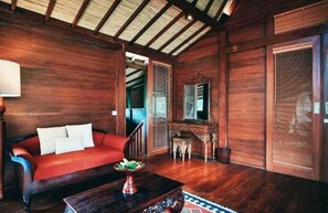 A wooden-floored room with a red sofa, a small table with a plant, and a mirror above a wooden cabinet.