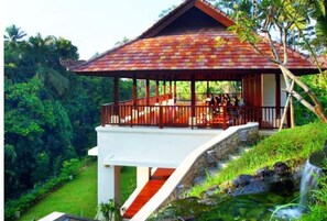 Set amidst lush greenery, this two-story building offers a serene escape with a covered outdoor area and a small water feature.