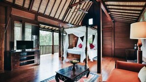 Um quarto espaçoso com teto de madeira, uma televisão sobre um suporte de madeira, uma cama branca com almofadas vermelhas e um sofá vermelho.
