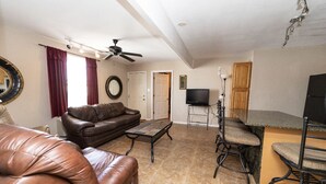 A living room with a brown leather couch, a coffee table, a TV, and a kitchen area with a bar and stools. - Whiskey Bay Lodge #3 (Boothville-Venice)