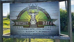 A sign for Whiskey Bay Lodge, listing amenities like 2 bedroom/2 bath, full kitchen, WiFi, 4 sleeps, and RV parking. - Whiskey Bay Lodge #3 (Boothville-Venice)