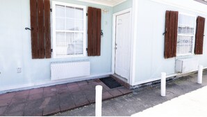 A small, single-story building with a light blue exterior, two windows with brown shutters, and a white door. - Whiskey Bay Lodge #3 (Boothville-Venice)
