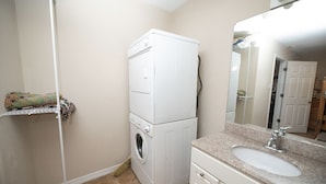 A compact bathroom with a white washing machine, a sink, and a mirror. - Whiskey Bay Lodge #3 (Boothville-Venice)