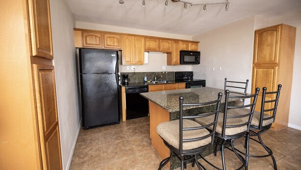 A kitchen with wooden cabinets, a black refrigerator, a microwave, a stove, and a dining area with four chairs. - Whiskey Bay Lodge #3 (Boothville-Venice)