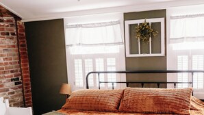 A bedroom with a bed, a ceiling fan, a window with sheer curtains, and a wall-mounted light fixture.