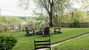A backyard with a table and chairs, a fire pit, and a view of a river and hills.