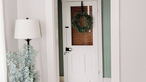 A hallway with a white door, a green door, a wreath, a lamp, and a potted plant.