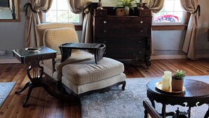 A cozy living room with a wooden ceiling, a sofa, a loveseat, a small table with candles, and a dresser with a mirror and a lamp.