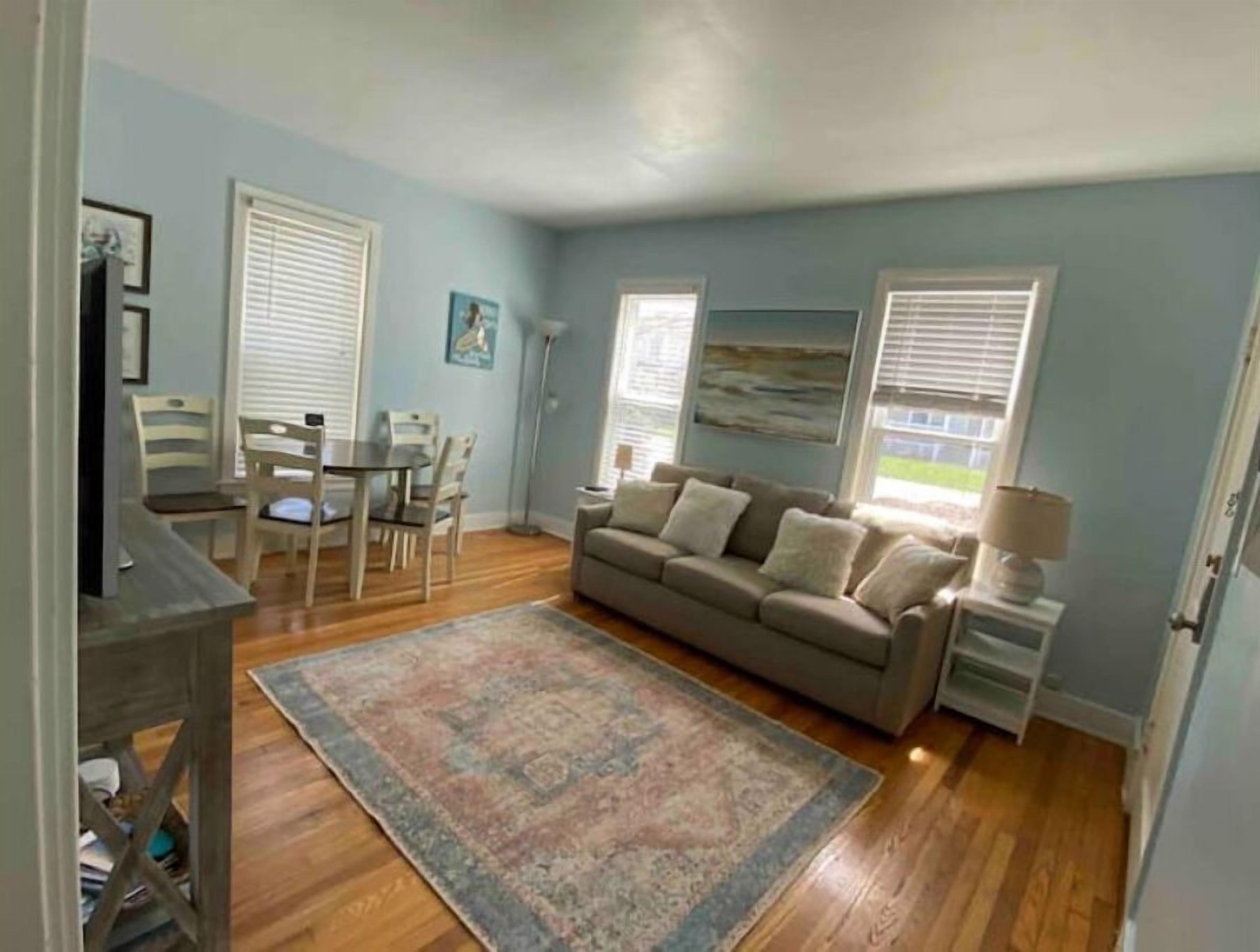 A living room with a beige sofa, a patterned rug, a dining table with chairs, and a floor lamp.