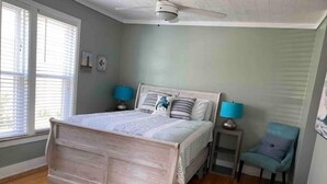 Een slaapkamer met een houten bed, twee nachtkastjes met lampen, een stoel en een plafondventilator.