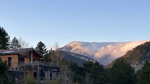 Una cabaña de madera con balcón, rodeada de un bosque denso y montañas.