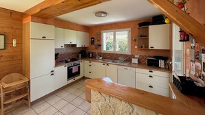 Cocina pequeña con vigas de madera, armarios blancos, estufa y lavabo.