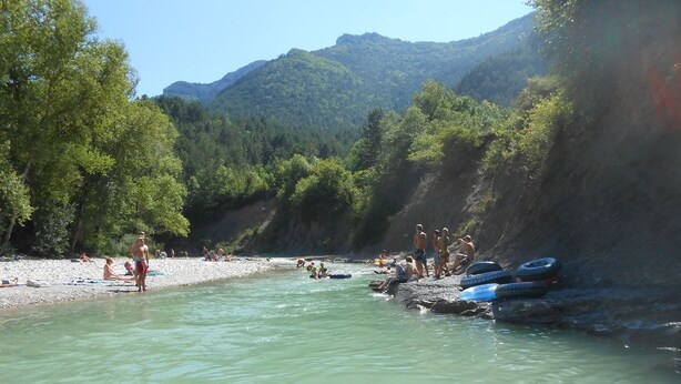 Un río con gente disfrutando de actividades acuáticas, rodeado de un paisaje rocoso y árboles.