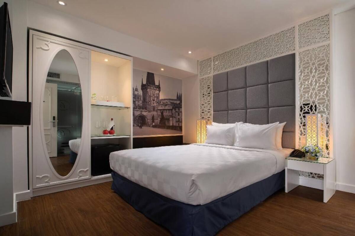 A hotel room with a large bed, a wardrobe with a mirror, a decorative wall panel, and a nightstand with a lamp.