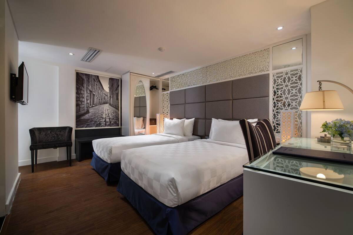 A hotel room with two beds, a desk, a chair, a TV, and a decorative wall.