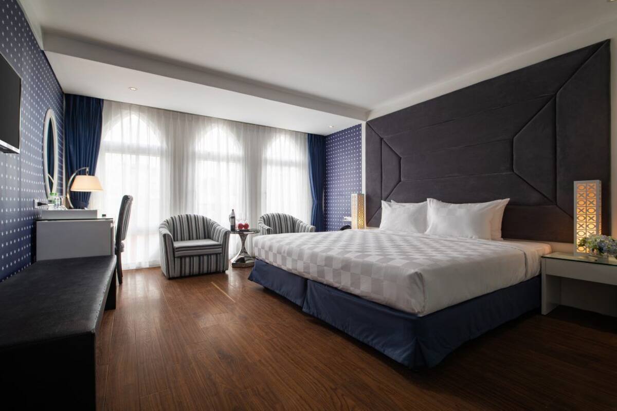 A modern hotel room with a large bed, a desk, a chair, and a vanity with a mirror.