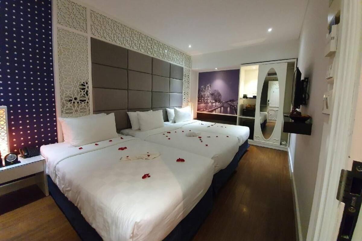 A hotel room with a large bed, a nightstand, a mirror, and a view of a cityscape.