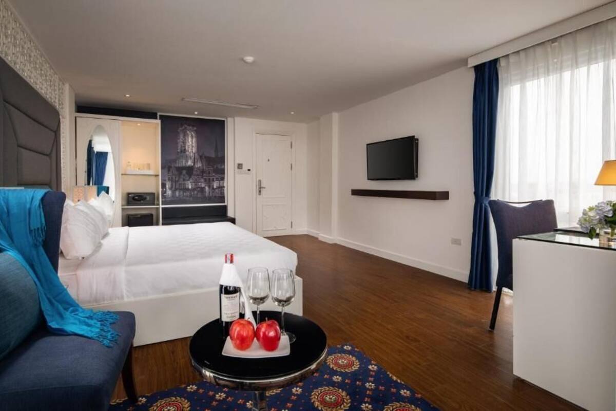 A hotel room with a bed, a sofa, a desk, a TV, and a cityscape view.