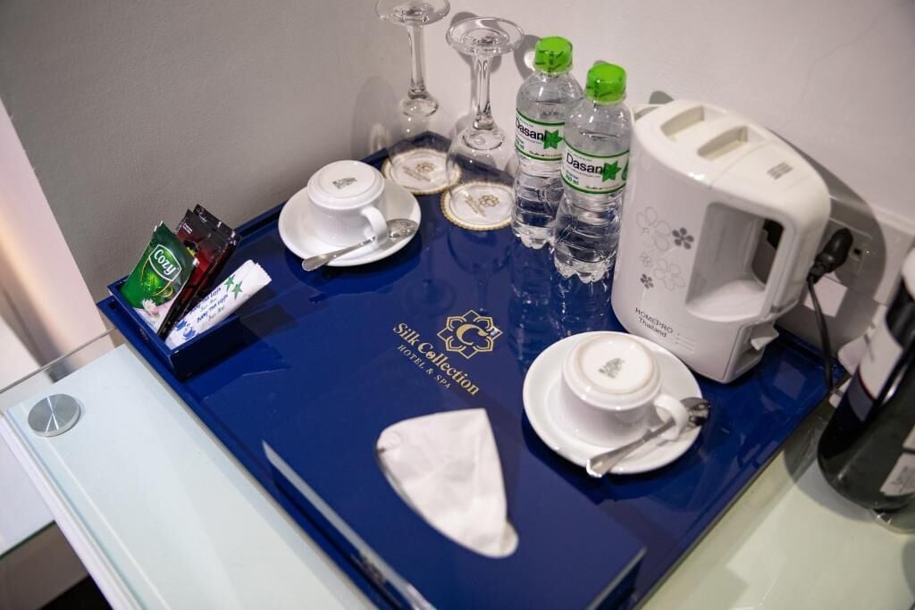 Dans une chambre d'hôtel, on trouve un mini-bar avec un plateau bleu, des sachets de thé, des bouteilles d'eau, des verres et un grille-pain.