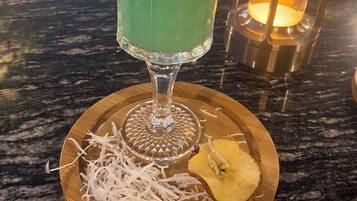 A cocktail in a glass with a lime garnish, served on a wooden coaster with shredded white material and a pineapple slice.