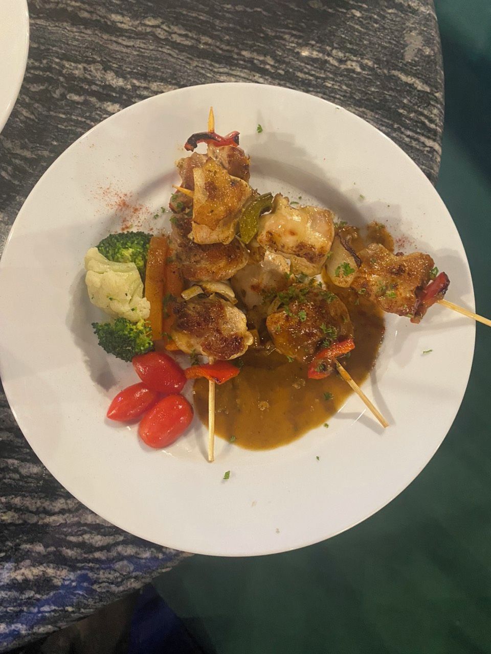A plate of skewered meat with vegetables and sauce.
