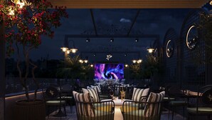 An outdoor seating area with a large screen displaying a space-themed image, surrounded by chairs and tables. - Victor Metropolis Hotel & Rooftop bar (Hanoi)