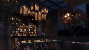 An outdoor bar area with a wooden table and chairs, a bar stocked with bottles, and a decorative tree with flowers. - Victor Metropolis Hotel & Rooftop bar (Hanoi)