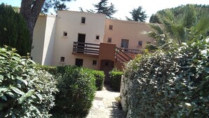 Un camí que condueix a un edifici de diverses plantes amb balcons i una entrada tancada per una reixa.