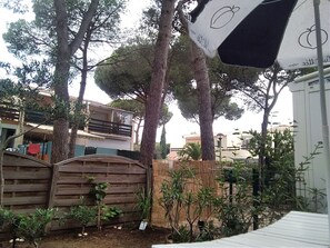 A garden area with a wooden fence, trees, and a white structure with a black and white design. - Studio Cabine Avec Jardin, Piscine à Côté du Village Naturiste (Agde)