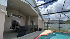 Ein überdachter Außenbereich mit Pool, einer Terrasse mit Stühlen und einem Deckenventilator.