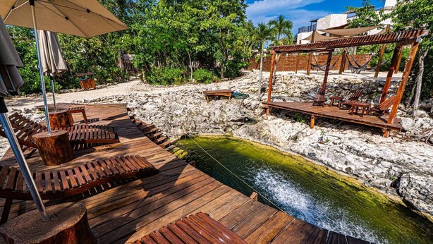 Una terraza de madera con sillones de descanso y una piscina pequeña, rodeada de un paisaje pedregoso y vegetación.