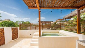 Un área de spa al aire libre con bañera de hidromasaje, pérgola de madera y una estructura con techo de paja.