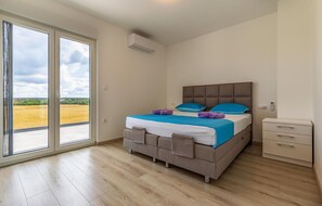 Un dormitorio con cama, mesita de noche, cómoda y puerta corrediza de vidrio que da a un balcón.