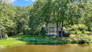 A house surrounded by lush greenery and a pond. - Family-sized Cozy Cottage - mountains views, fishing, & hot tub, in Suches, GA (Suches)