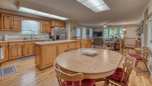 A spacious kitchen with wooden cabinets, a central island, and a dining area with a round table and chairs. - Family-sized Cozy Cottage - mountains views, fishing, & hot tub, in Suches, GA (Suches)