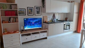 Una cocina moderna con armarios blancos, horno empotrado y televisor sobre un mueble de madera.