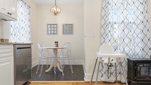 Una cocina con mesa, sillas, una trona blanca, estufa y una lámpara colgante.