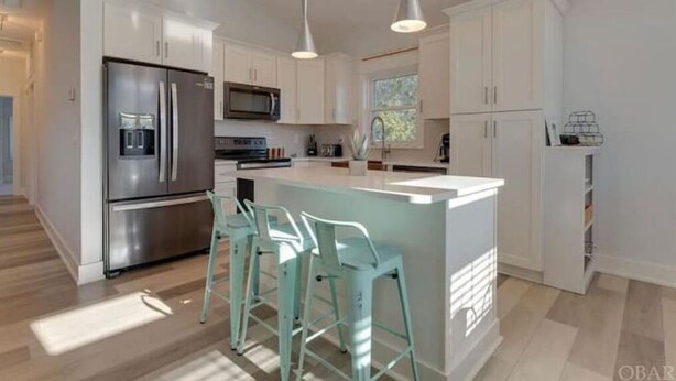 A modern kitchen with white cabinetry, stainless steel appliances, and a central island with bar stools.
