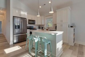 Une cuisine moderne avec des meubles blancs, des appareils en acier inoxydable et un îlot central doté de tabourets de bar.